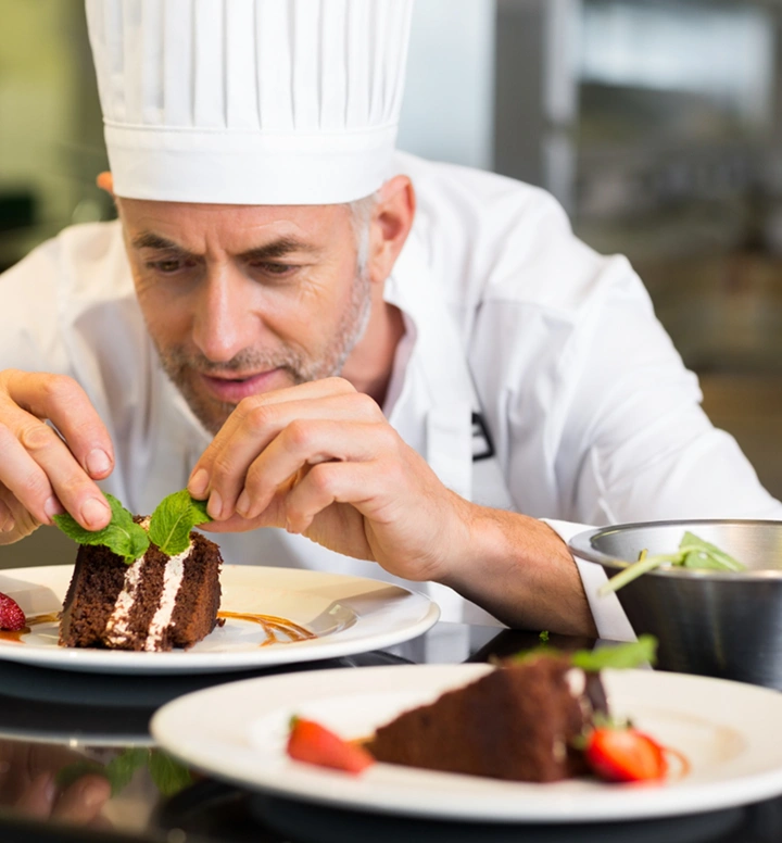 Professionele chef die zorgvuldig een stuk chocoladetaart versiert met verse muntblaadjes in een moderne keukenomgeving