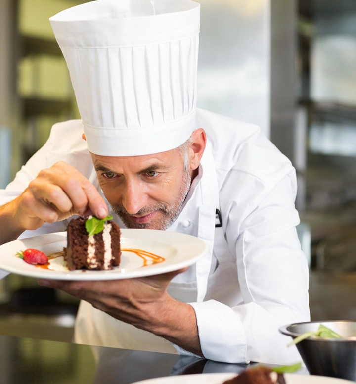 Professionele chef die zorgvuldig een chocoladedessert versiert met verse muntblaadjes voor het serveren in een moderne keuken