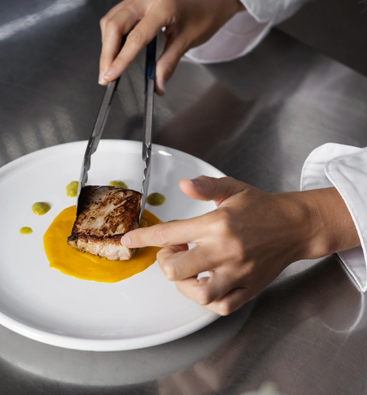 Chef plaatst zorgvuldig een gegrild visfilet op saus met een precieze fine dining presentatie techniek