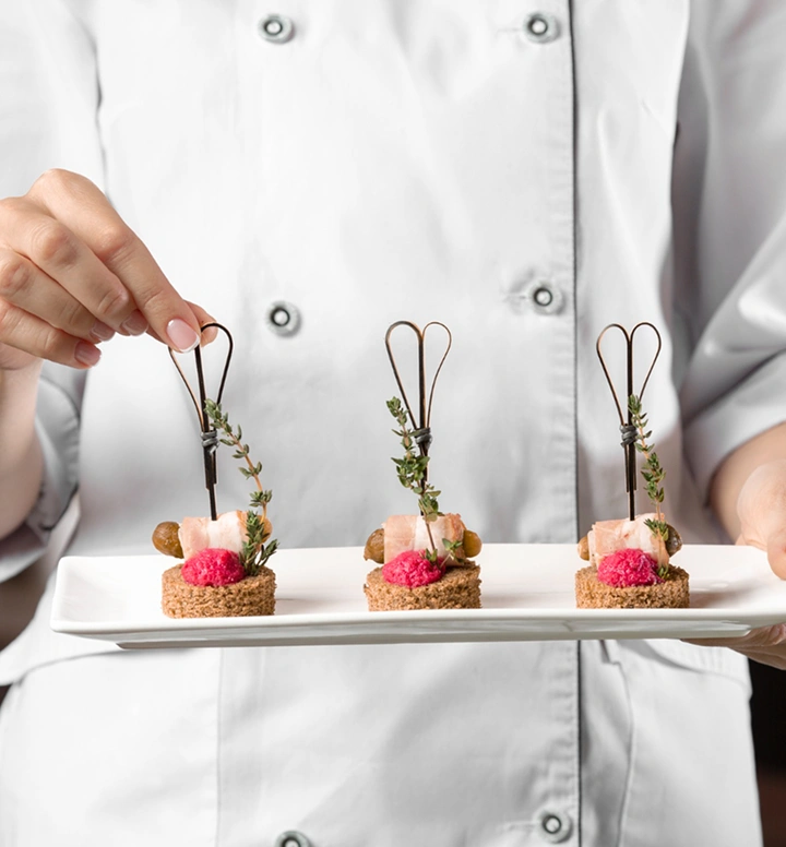 Chef houdt een bord met elegante mini-canapés, gegarneerd met kruiden en bessen, klaar voor verfijnde cateringservice