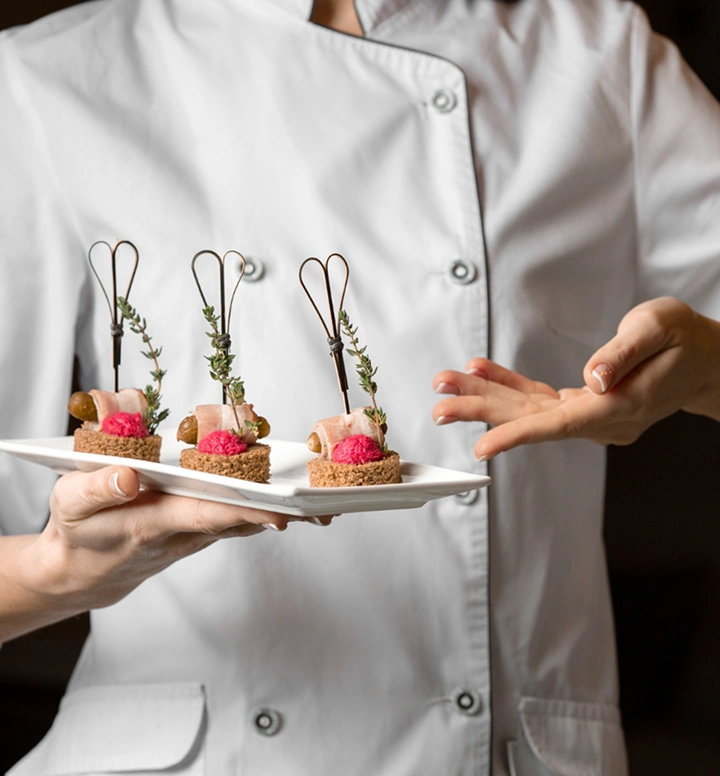 Chef houdt een bord met verfijnde mini-canapés, gegarneerd met kruiden en bessen, klaar voor een verfijnde presentatie