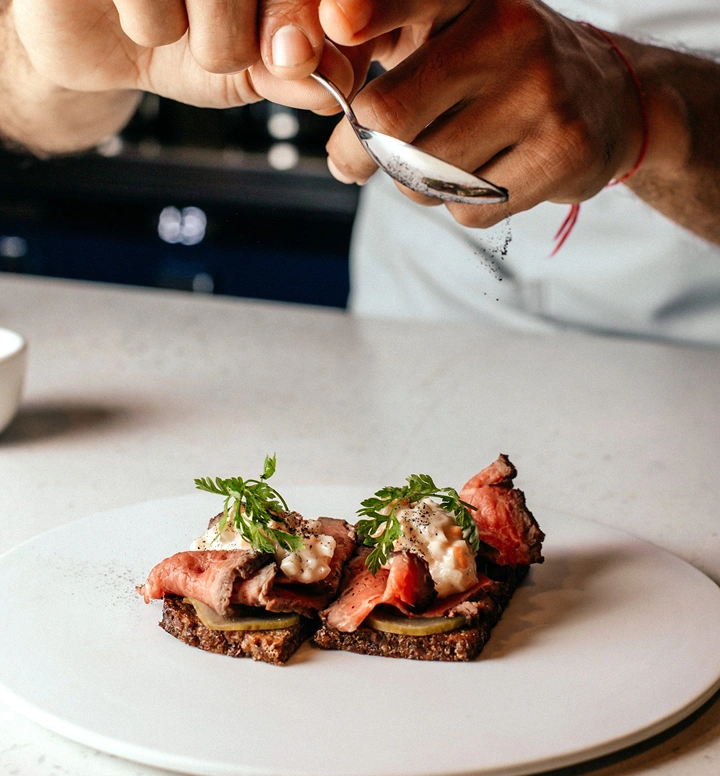 Chef strooit kruiden over gourmet zalmcanapés geserveerd op geroosterd brood met kruiden op een wit bord in een moderne keuken