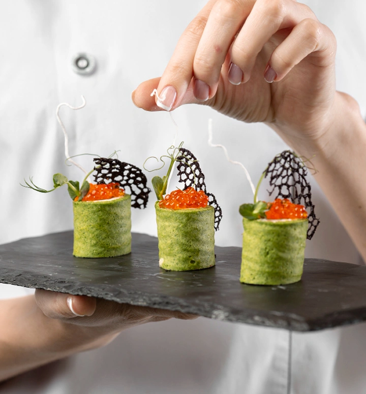 Chef presenteert elegante groene canapéhapjes, getopt met kaviaar en decoratieve garnering op een zwart serveerbord