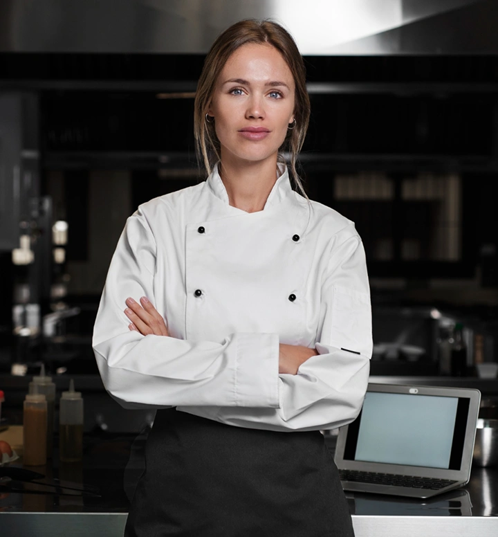 Professionele vrouwelijke chef staat zelfverzekerd met gekruiste armen in een moderne commerciële keukenomgeving